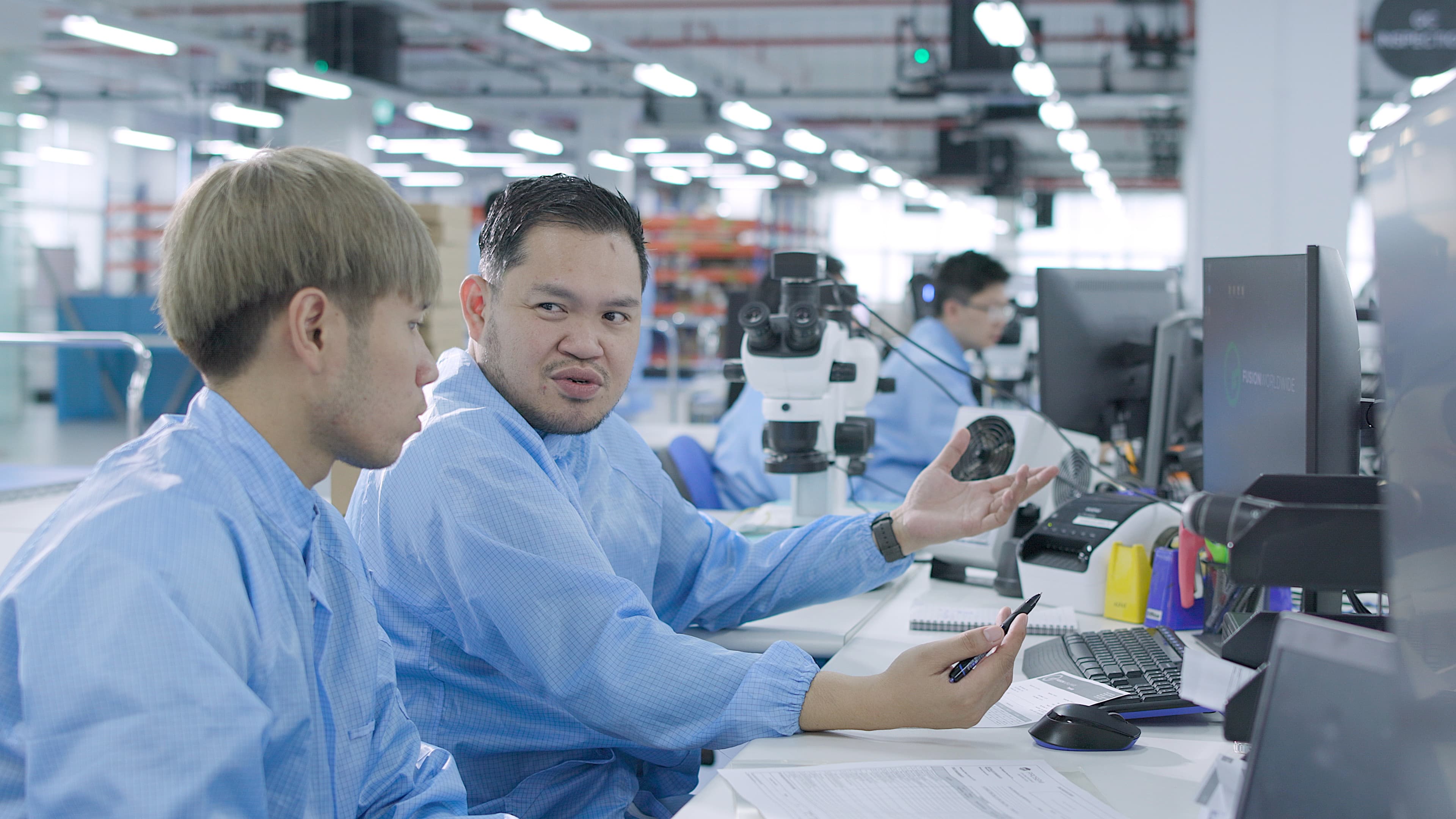 Two Fusion Worldwide engineers talking at their desks