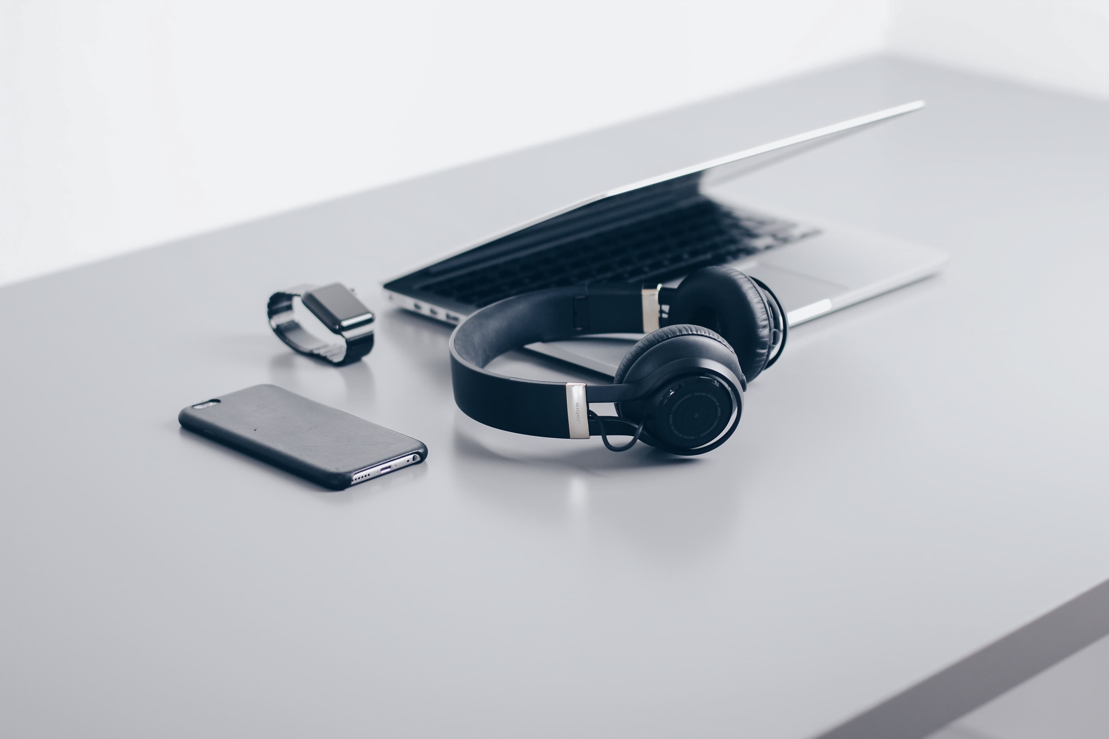 A phone, watch, headphones and laptop on a white desk