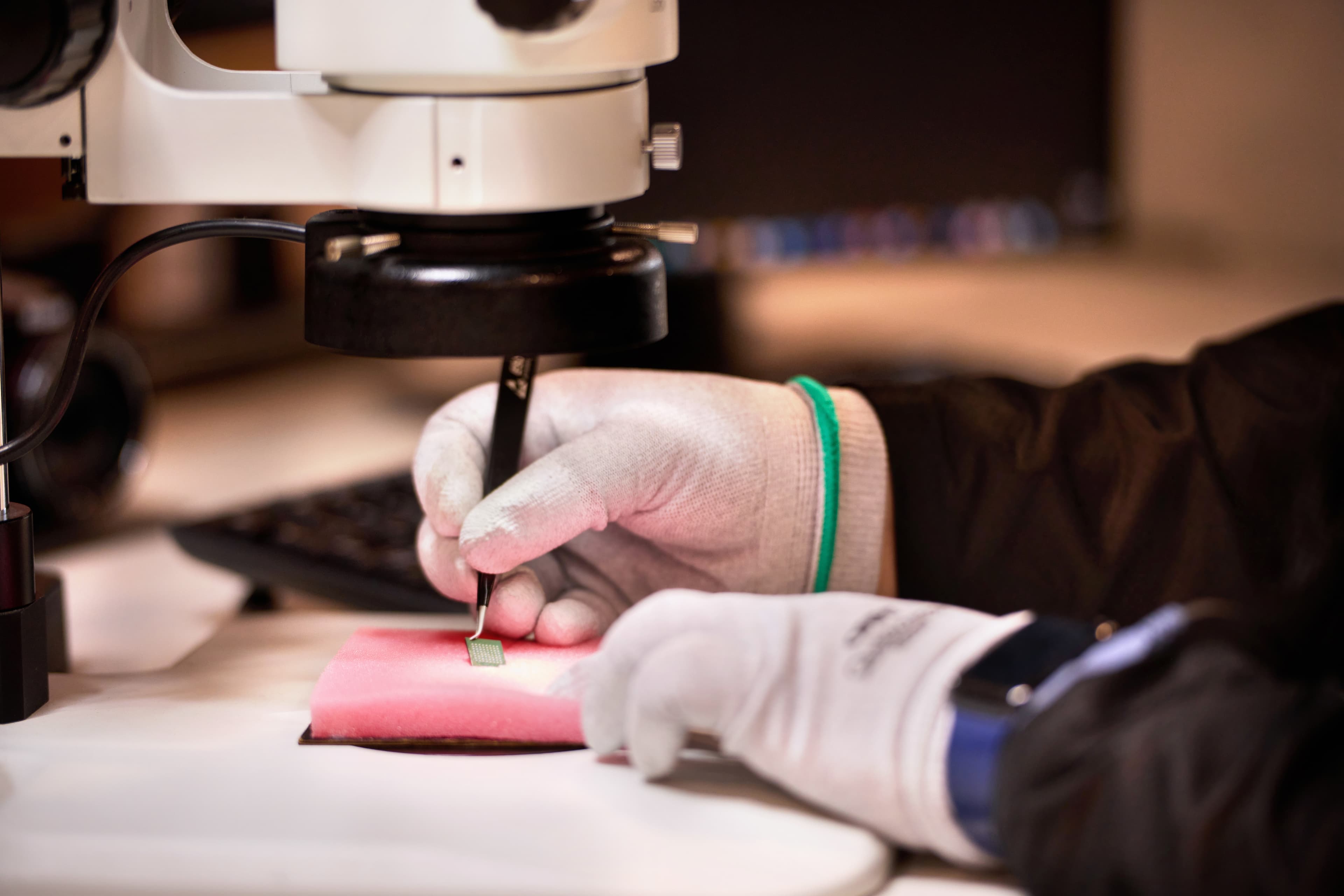 Gloved hands performing an inspection test on an electronic component under magnification